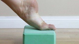 A person 's foot is resting on a green yoga block.
