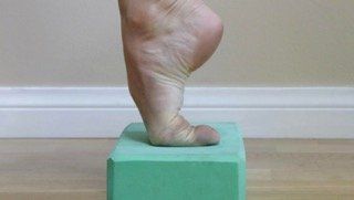 A person 's foot is standing on a green block.