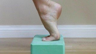 A person 's foot is standing on a green block.