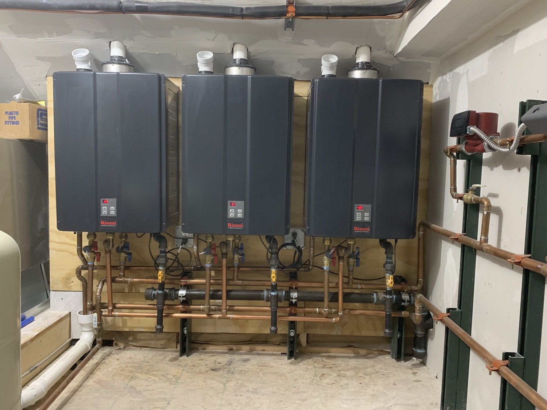The image displays a professional installation of three commercial-grade Rinnai tankless water heaters.