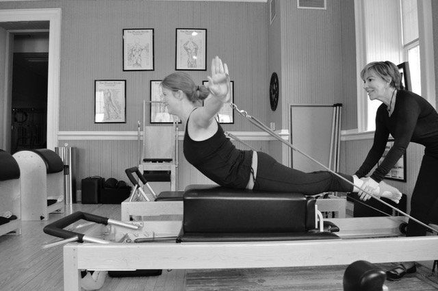 A woman is doing pilates on a machine while a teacher watches.