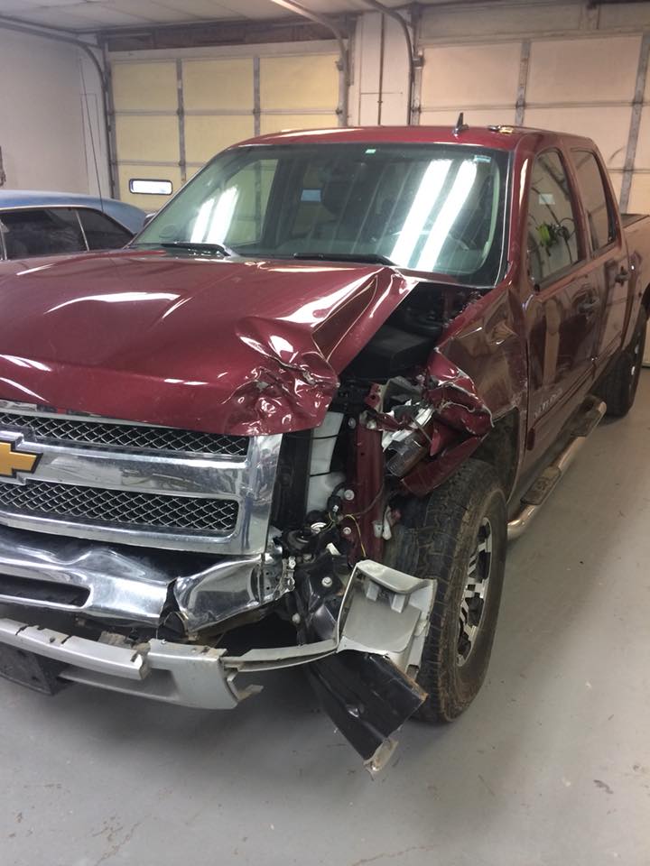 Damaged maroon pickup truck with front-end collision damage in a garage