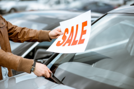 Person placing a white “SALE” sign on a car windshield at a dealership