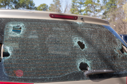 Rear windshield shattered with multiple bullet holes on a dark vehicle outdoors