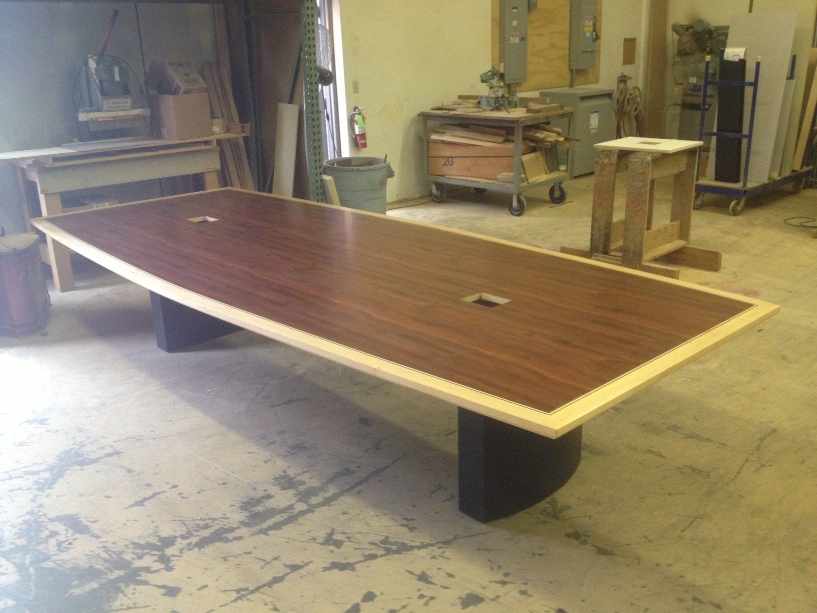 Large mahogany conference table with two circular cutouts, in a workshop.