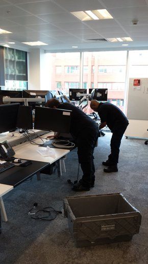 Two men are bending over a desk in an office.