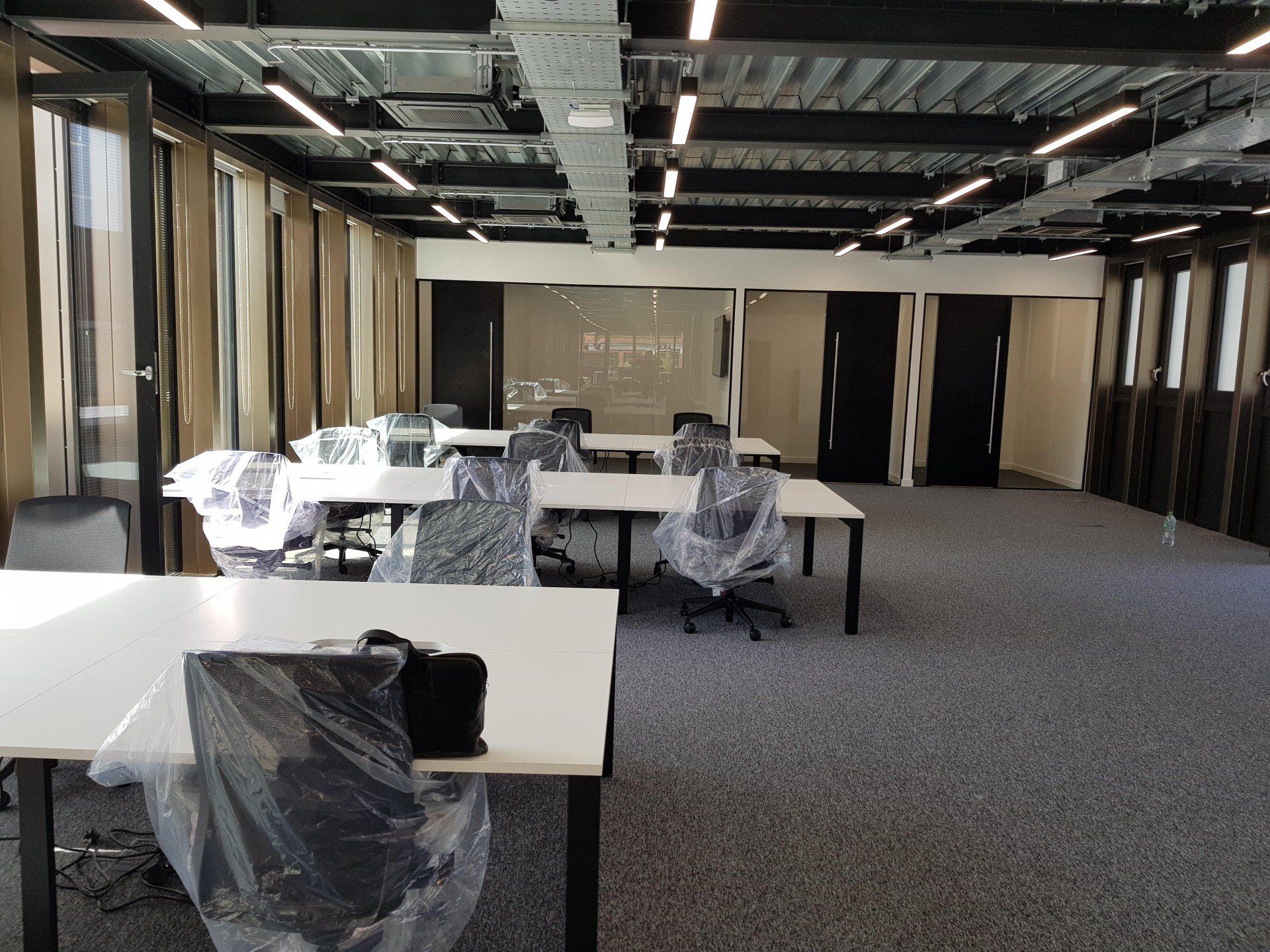 A large empty office with tables and chairs wrapped in plastic.