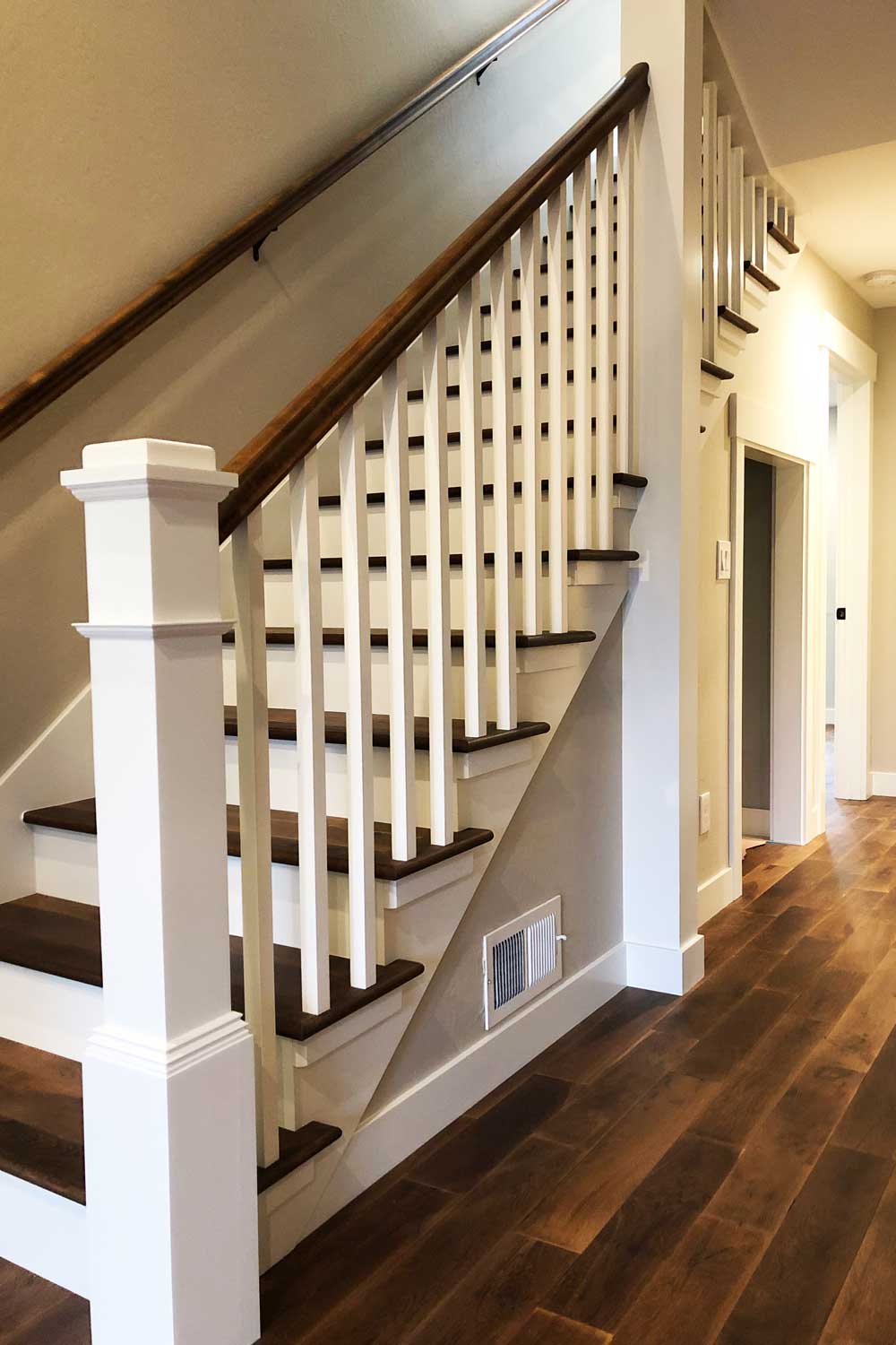 Interior staircase with newel posts and square balusters in white and wood stained railings and treads