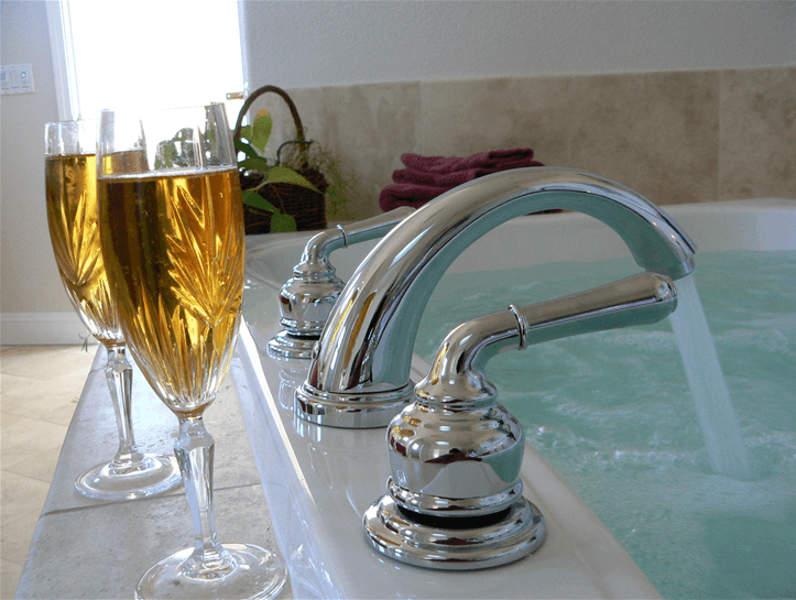 Close up of wine glasses sitting on the edge of a custom stone bathtub