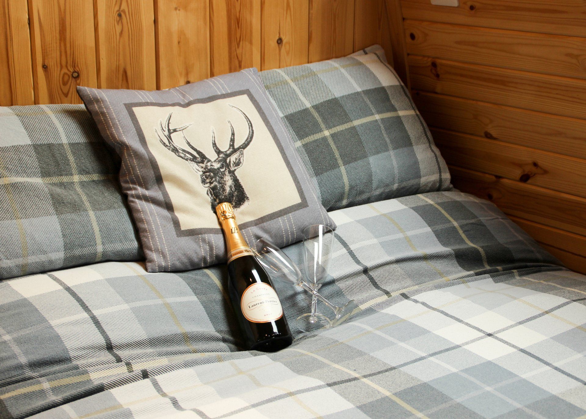 A bottle of champagne is sitting on a bed next to a pillow with a deer on it.