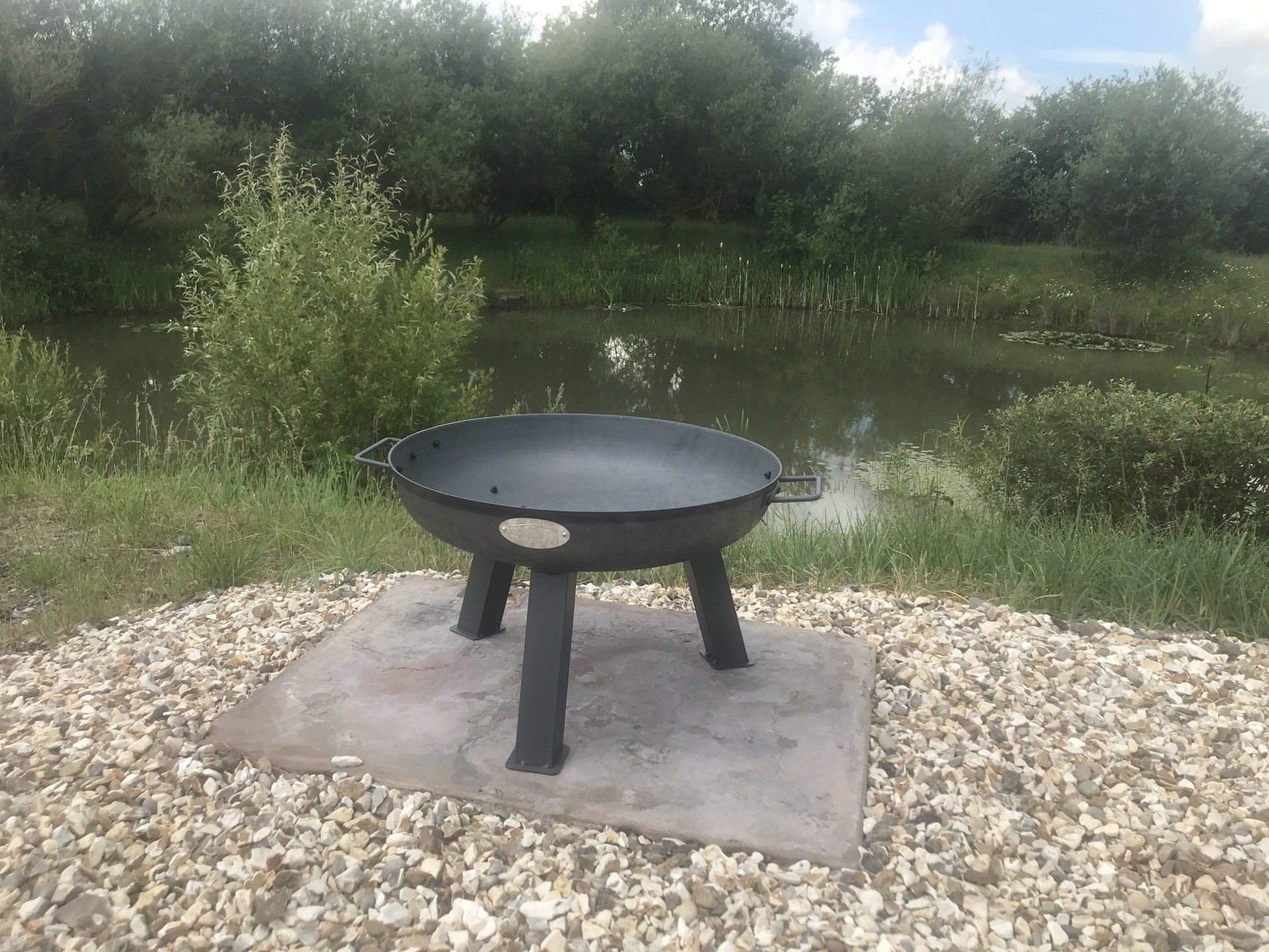 A fire pit is sitting on top of a pile of gravel next to a body of water.