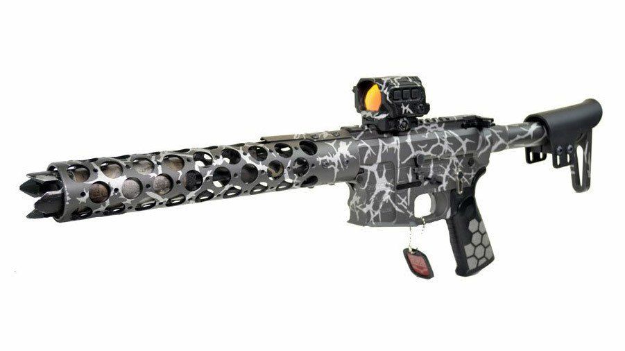 A long, silver and black rifle with red dot sight and a custom perforated barrel.