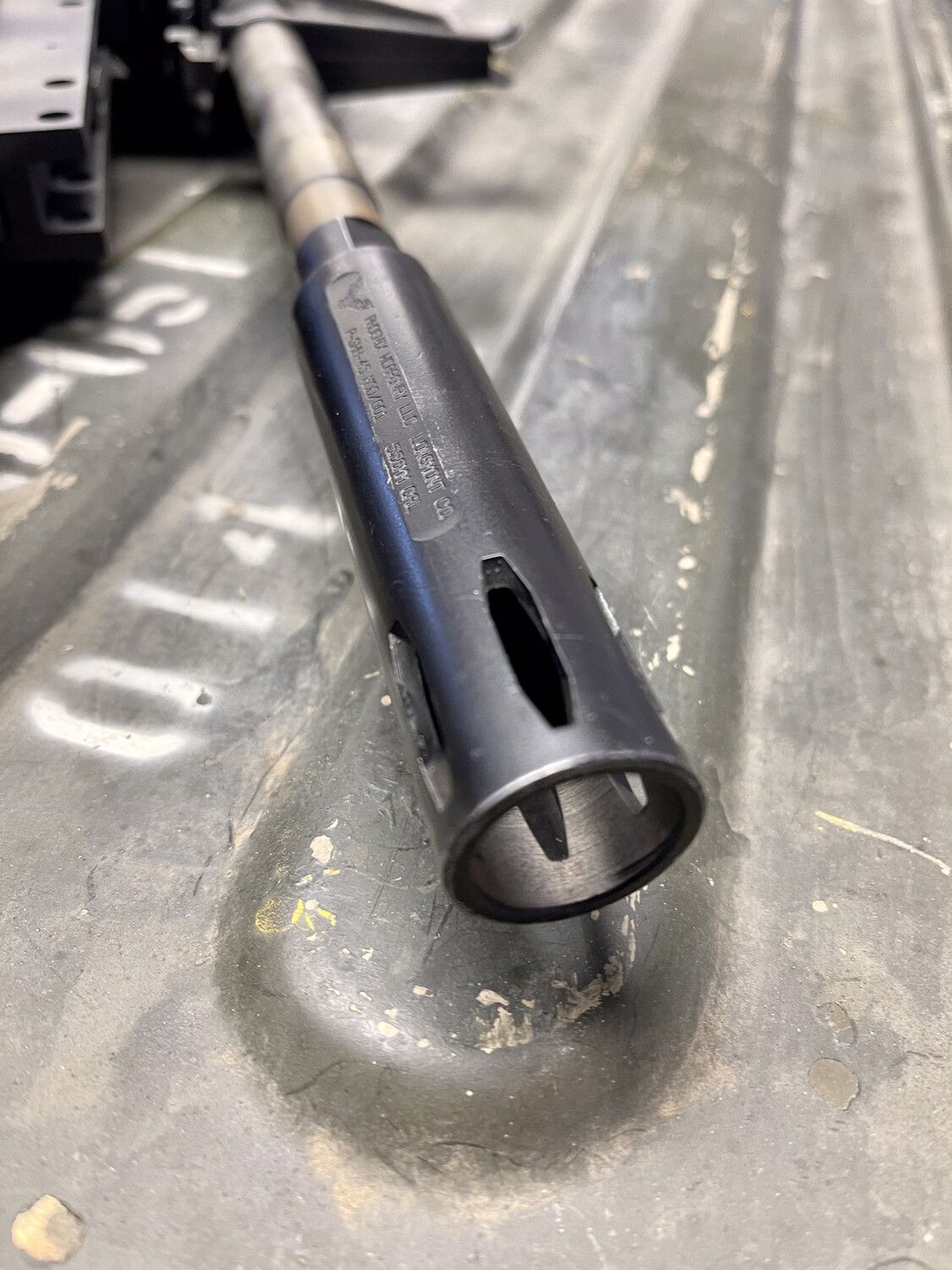 Black rifle barrel with a slotted muzzle, resting on a green surface.