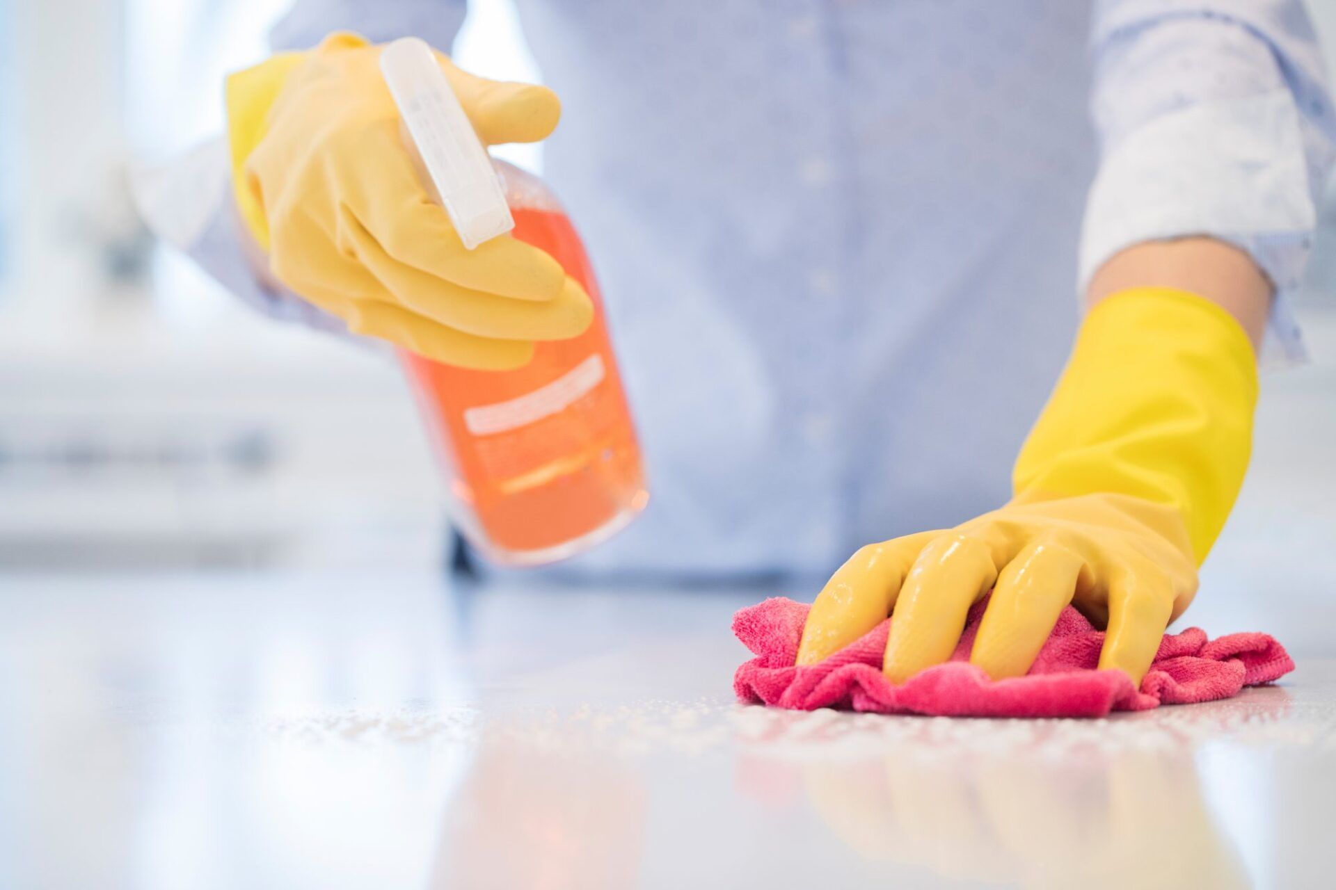 Person wearing yellow gloves sprays and wipes a counter with a pink cloth.