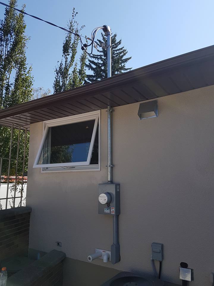 An outdoor utility wall with an electrical meter, a service conduit extending to the roof, and an open window.