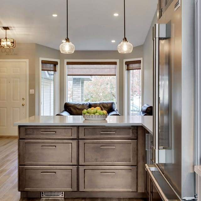 A kitchen island with dark cabinets and a white countertop, featuring pendant lights and a bowl of apples in the background.