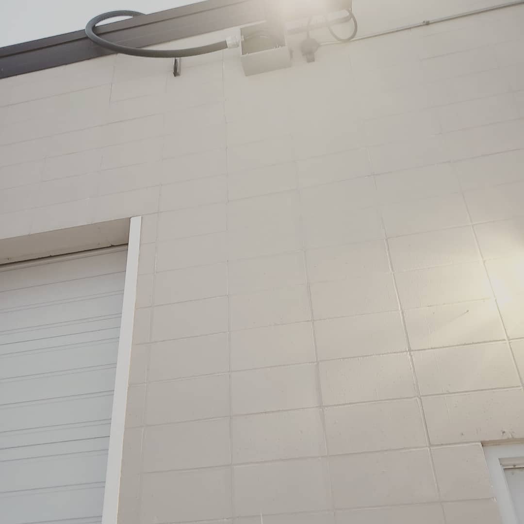 Exterior wall of a white concrete block building with a metal garage door and an exposed black utility pipe on the top edge.