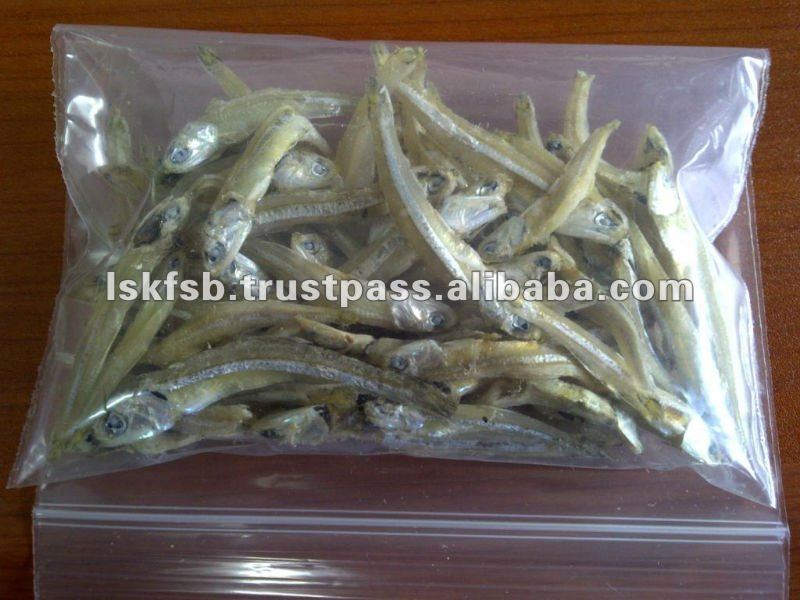 Dried anchovies in a clear plastic bag on a wooden surface.