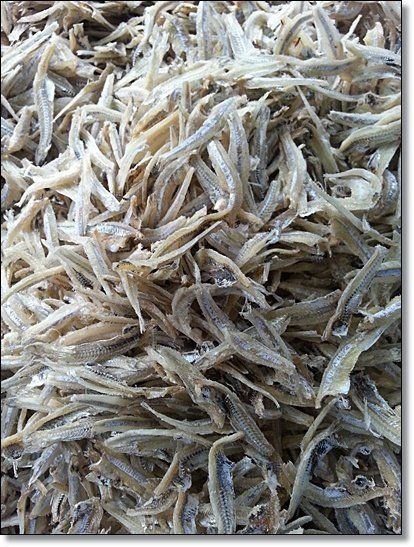 Pile of dried, small, silvery-tan fish, possibly anchovies, closely packed together.