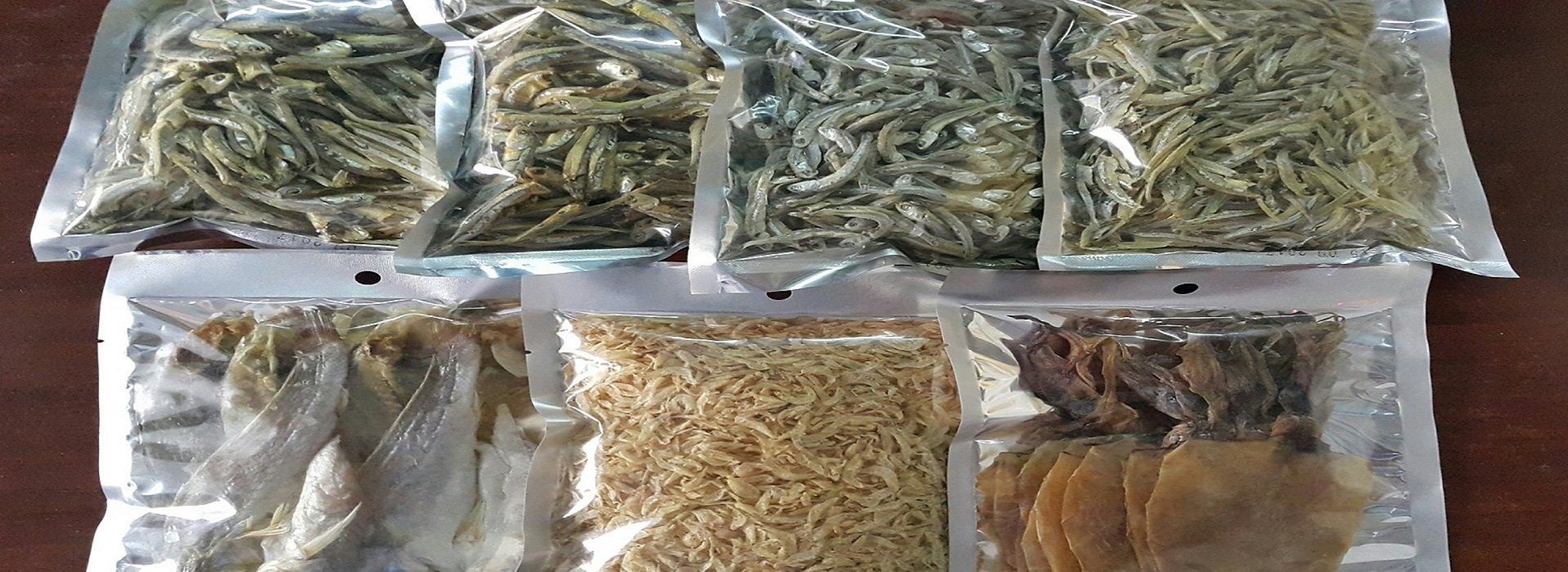 Bags of dried seafood products, including fish and squid, are arranged on a dark wooden surface.