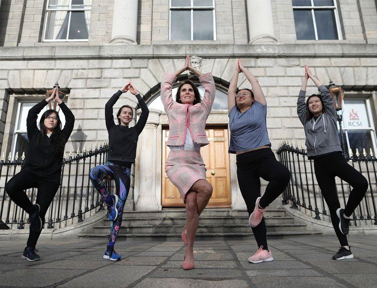 Five people pose in tree yoga poses outside a stone building with a wooden door.