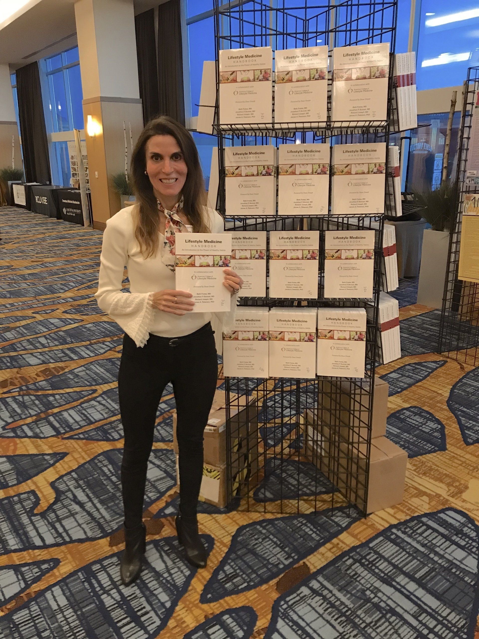 Woman holding a certificate beside a display of award plaques in a conference hall