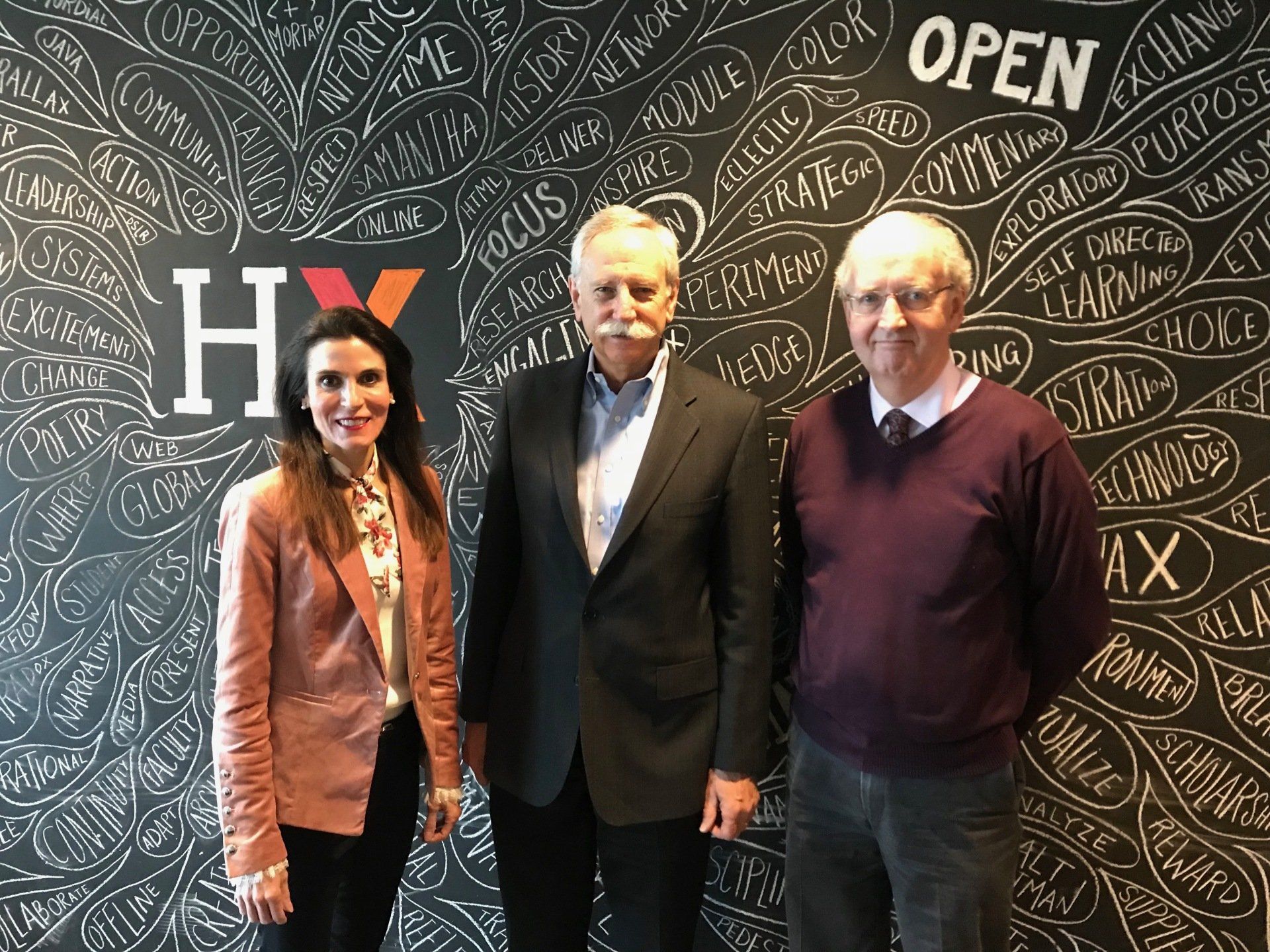 Three people posing in front of a chalkboard wall with “Hi” and “Open” written behind them.