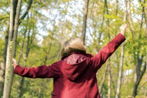 Person in a red jacket with arms outstretched in a sunlit forest