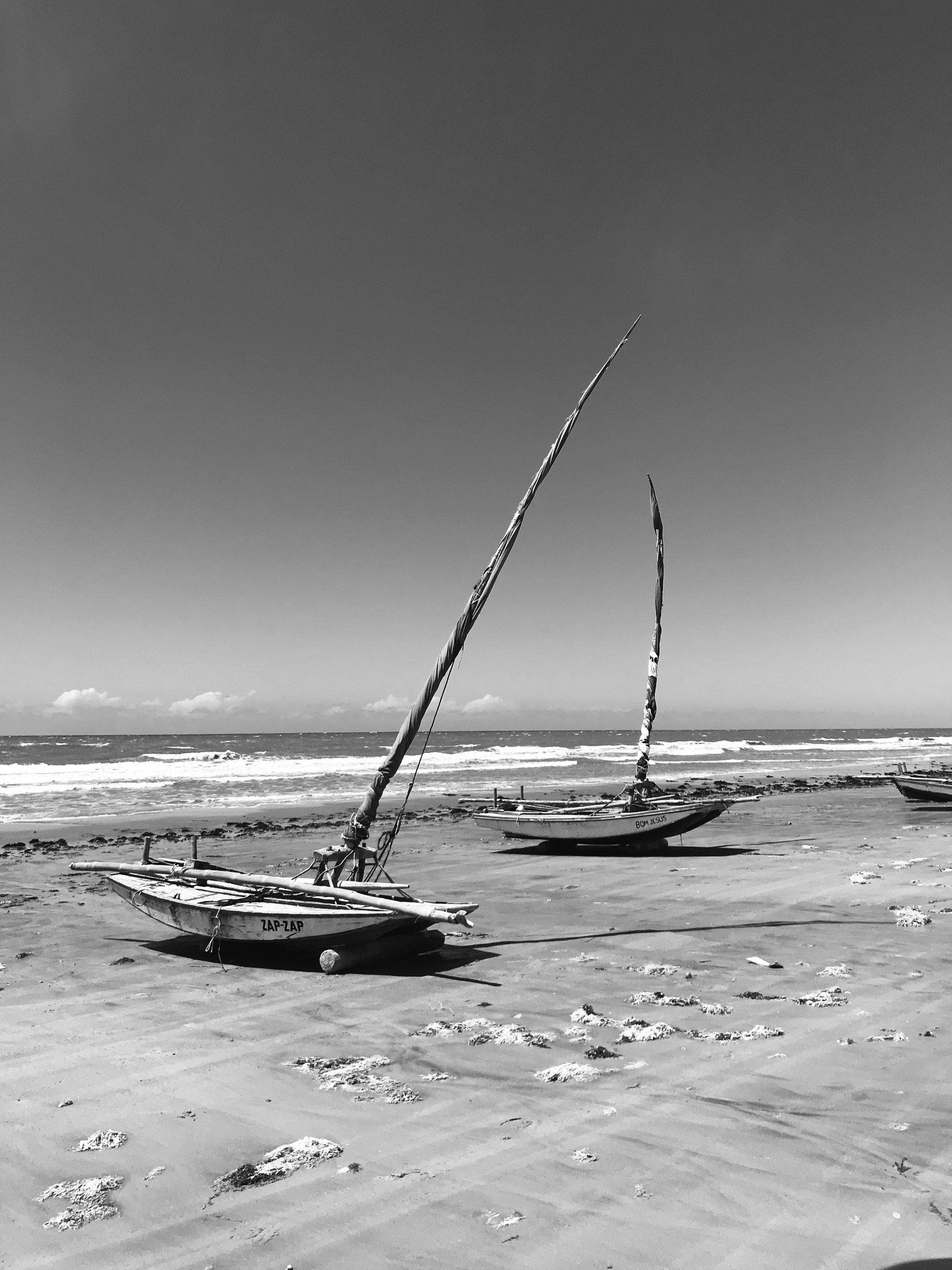 Duas jangadas, barcos de pesca tradicionais, repousam em uma praia de areia durante a maré baixa, sob um céu claro.