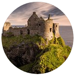 Ruínas do Castelo de Dunluce, empoleiradas na beira de um penhasco gramado com vista para o mar ao pôr do sol.