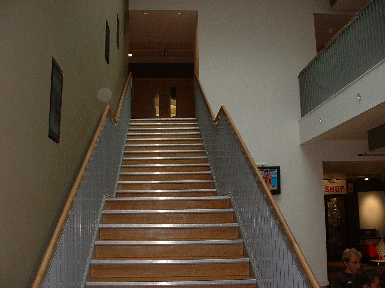Wooden staircase in a building with metal railings and cream walls. A doorway is at the top of the stairs.