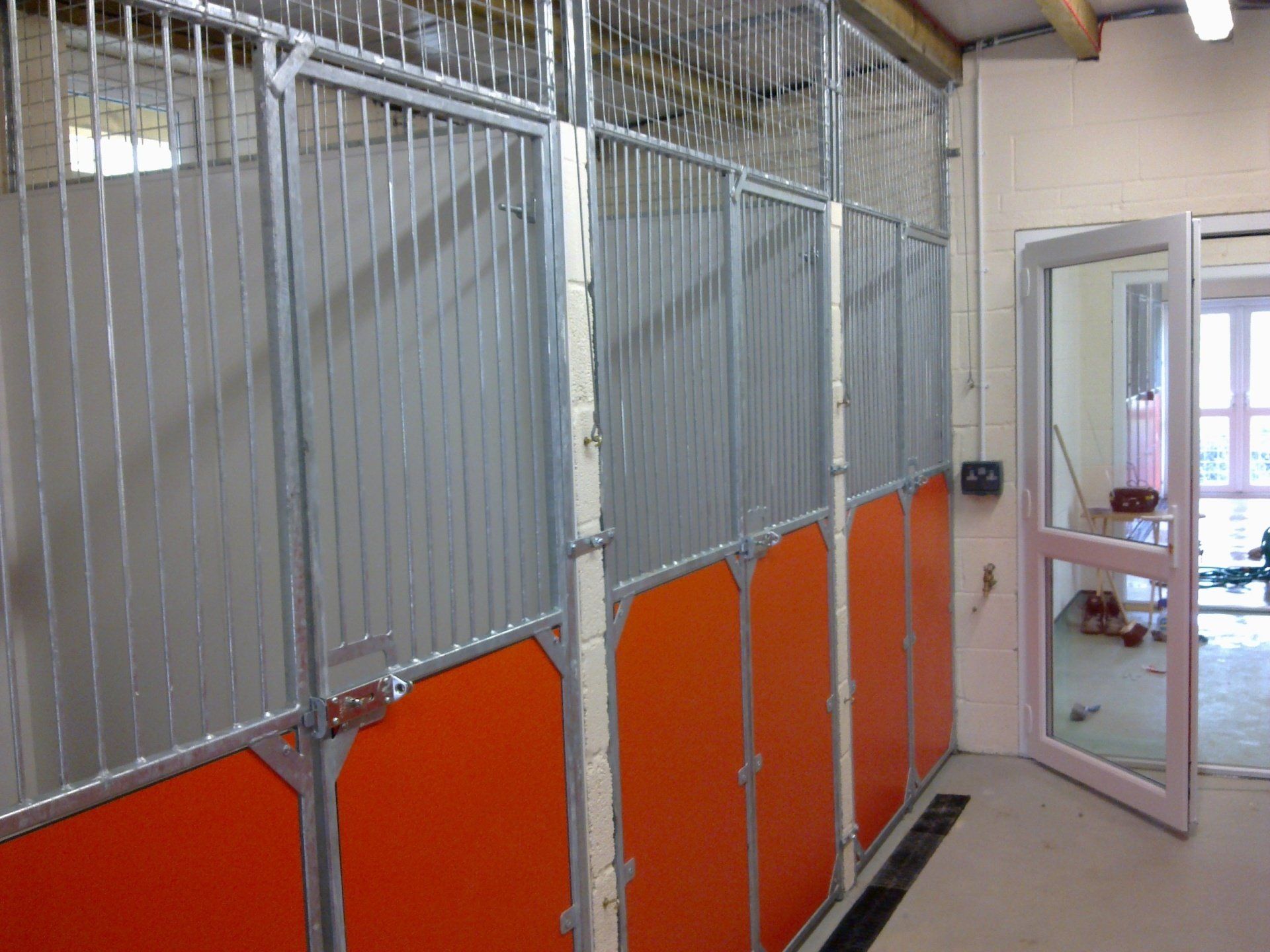 Stall partitions with orange lower panels and metal bars, next to an open door.