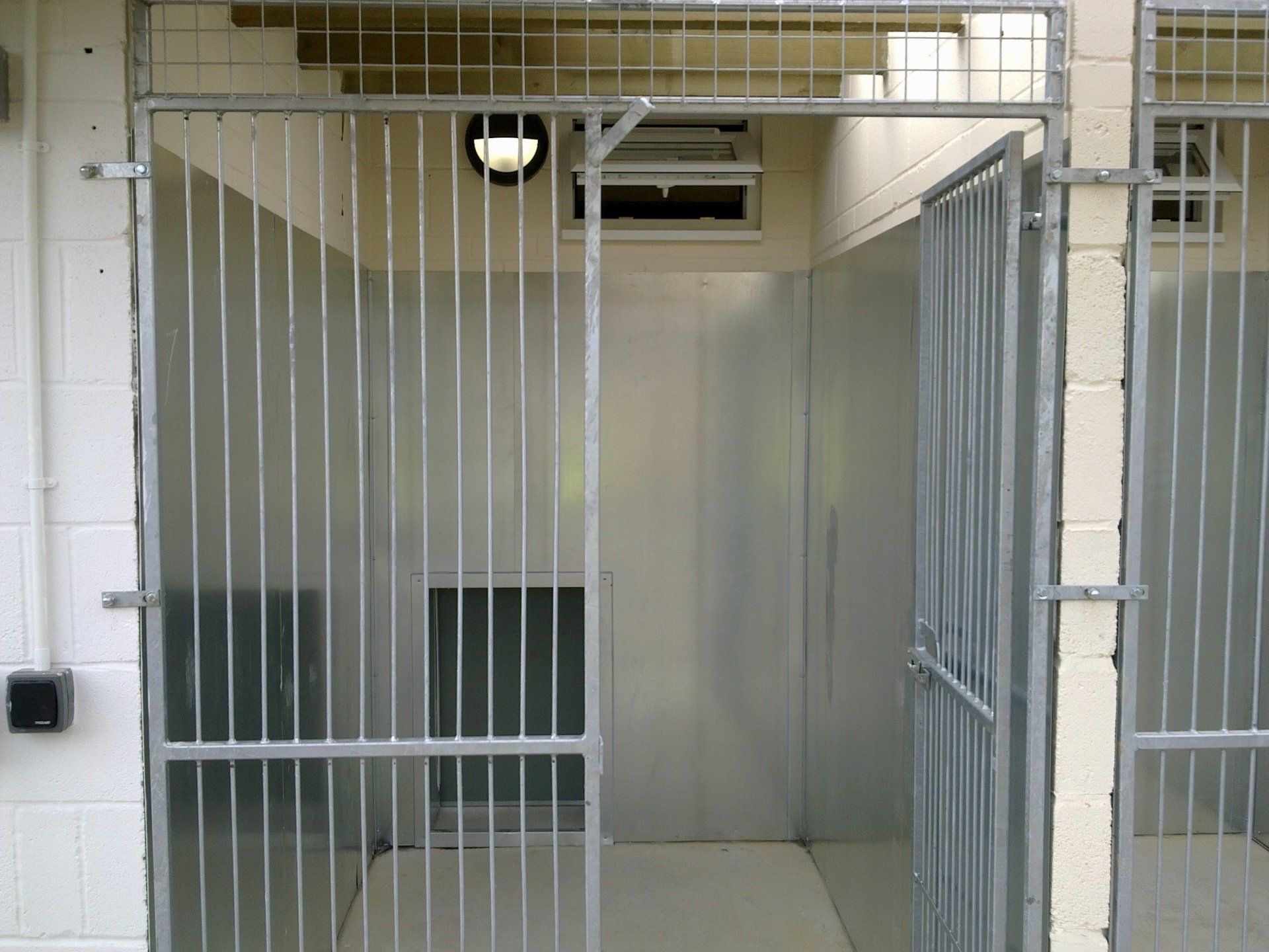 Metal dog kennel with open gate, interior view with light.