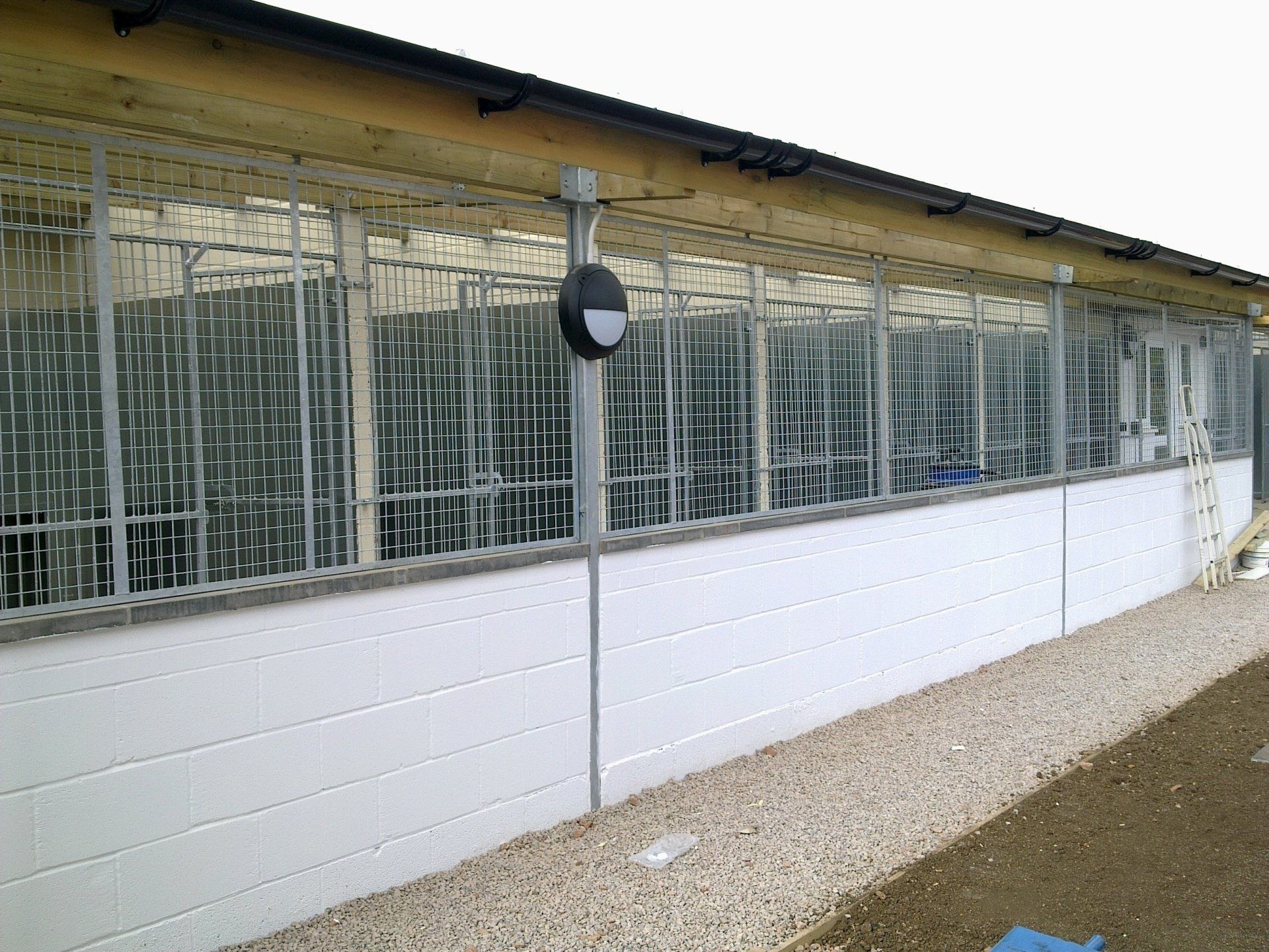 Exterior of a building with multiple caged sections, white siding, gravel ground, and a gray roof.