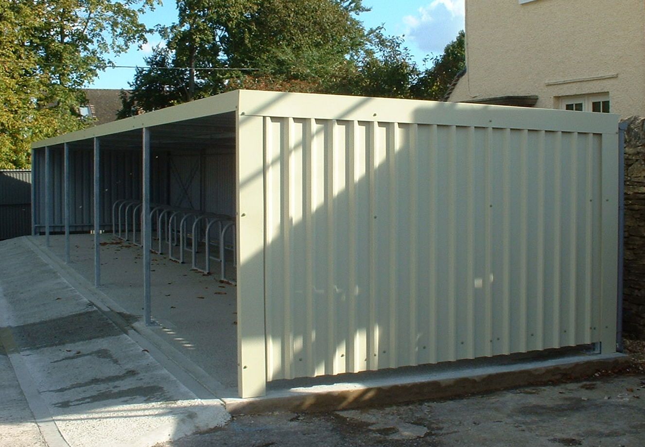 A covered bike rack made of corrugated metal panels in an outdoor setting.
