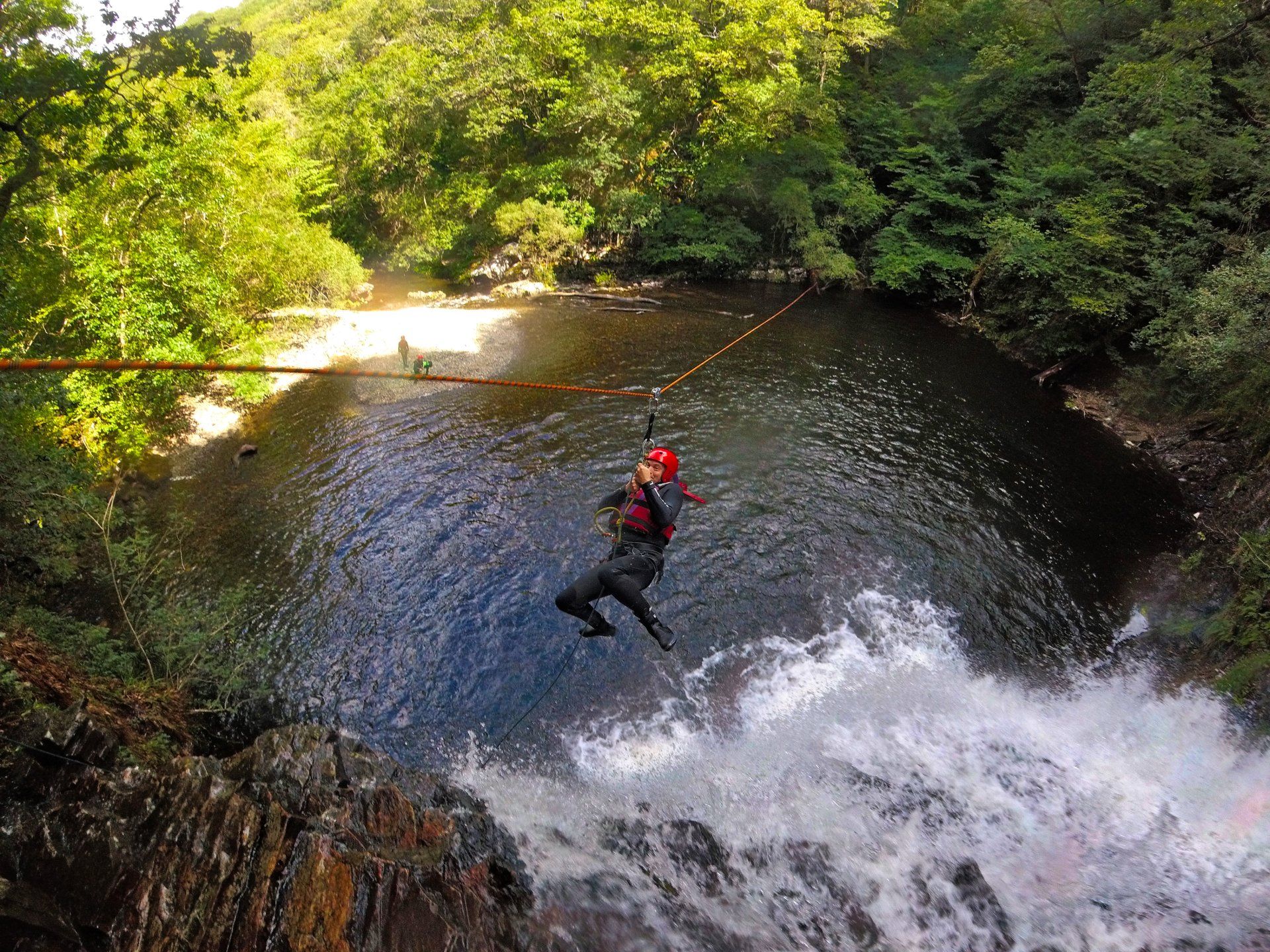Someone attached to a zip line half way down before landing in a pool at the bottom