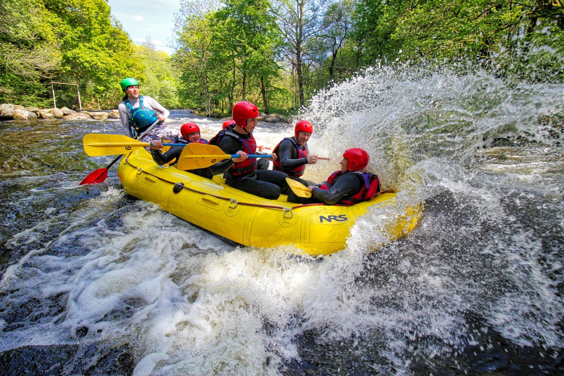 A bright yellow raft in a rapid with water spray over the front of the raft