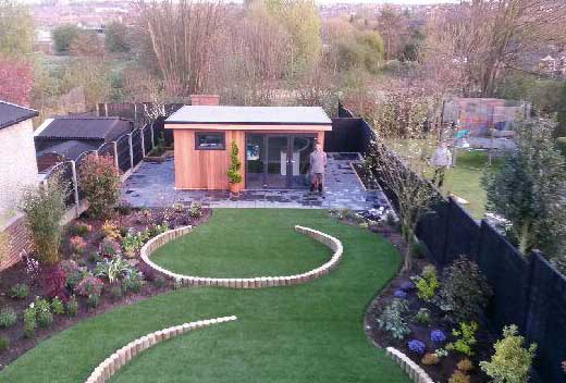 A large garden with a curved lawn and a shed at the end of it with trees and other gardens around it