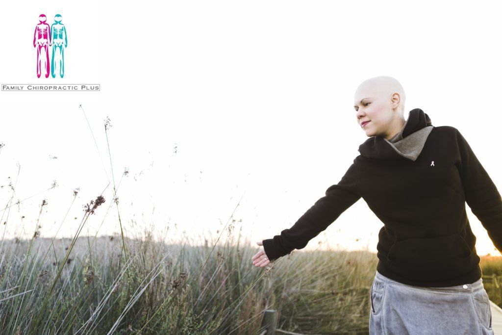 A woman with a bald head is standing in a field with her arms outstretched