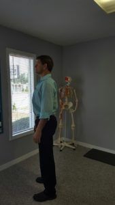 A man is standing in a room with a skeleton in the background.