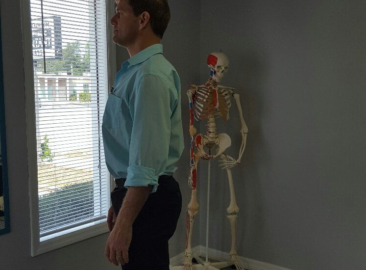 A man is standing in front of a skeleton in a room.