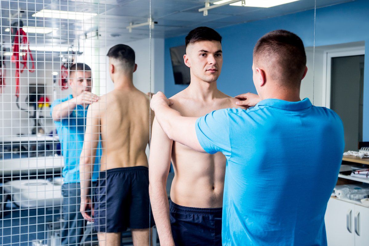A man is measuring another man 's shoulder in front of a mirror.
