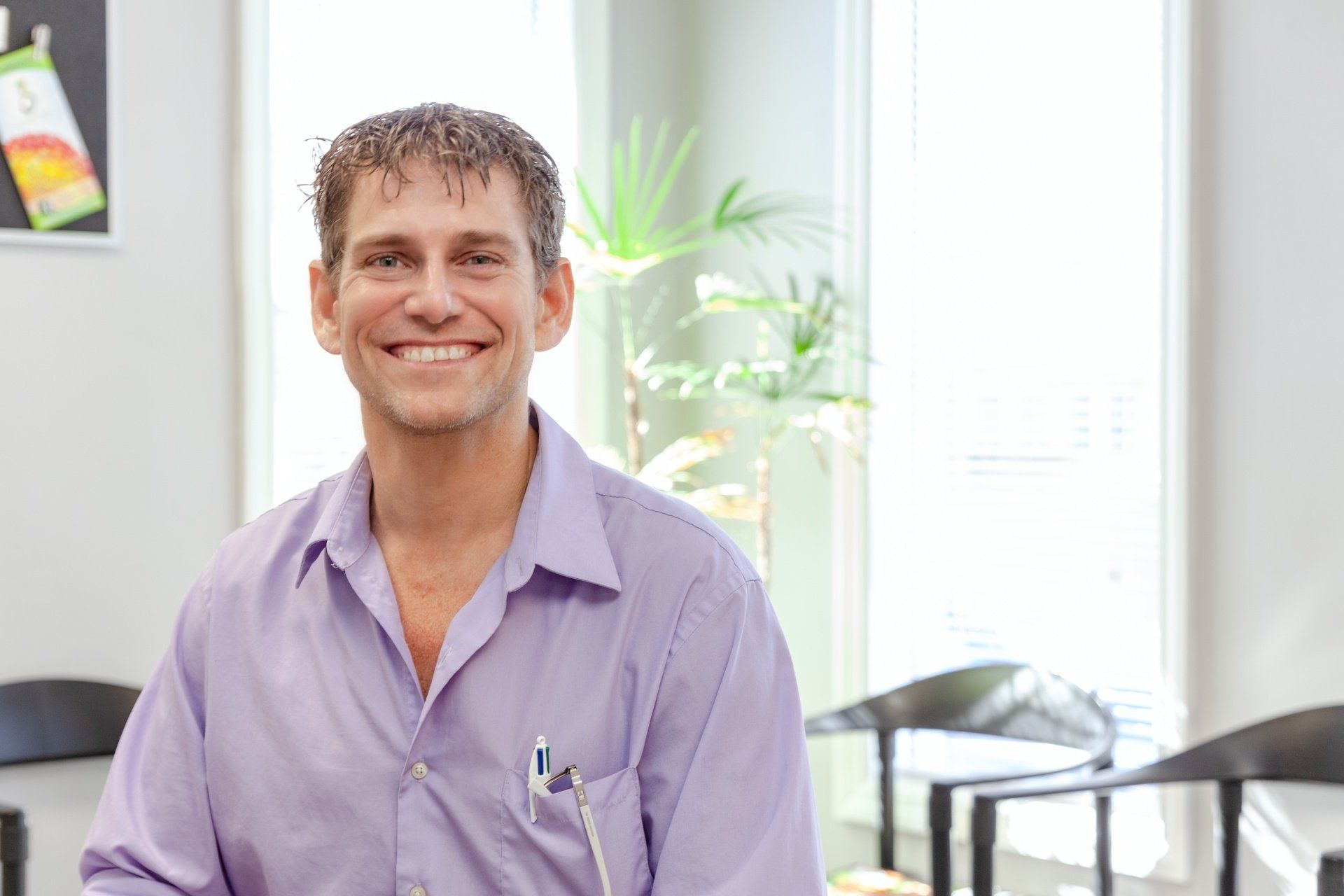 A man in a purple shirt is sitting in a waiting room and smiling.