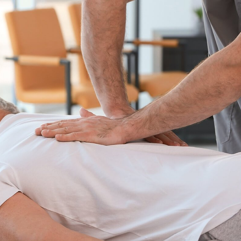A man is laying on a bed getting a massage from another man.