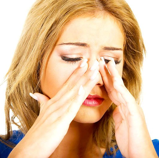 A woman in a blue shirt is covering her nose with her hands
