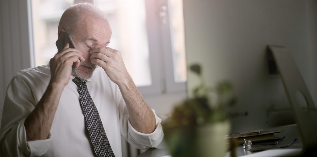 A man is rubbing his eyes while talking on a cell phone.