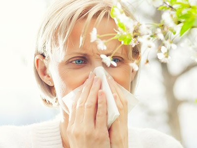 A woman is blowing her nose in front of a tree with flowers.