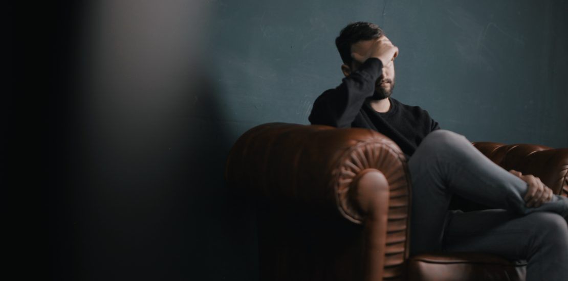 A man is sitting on a couch with his head in his hands.