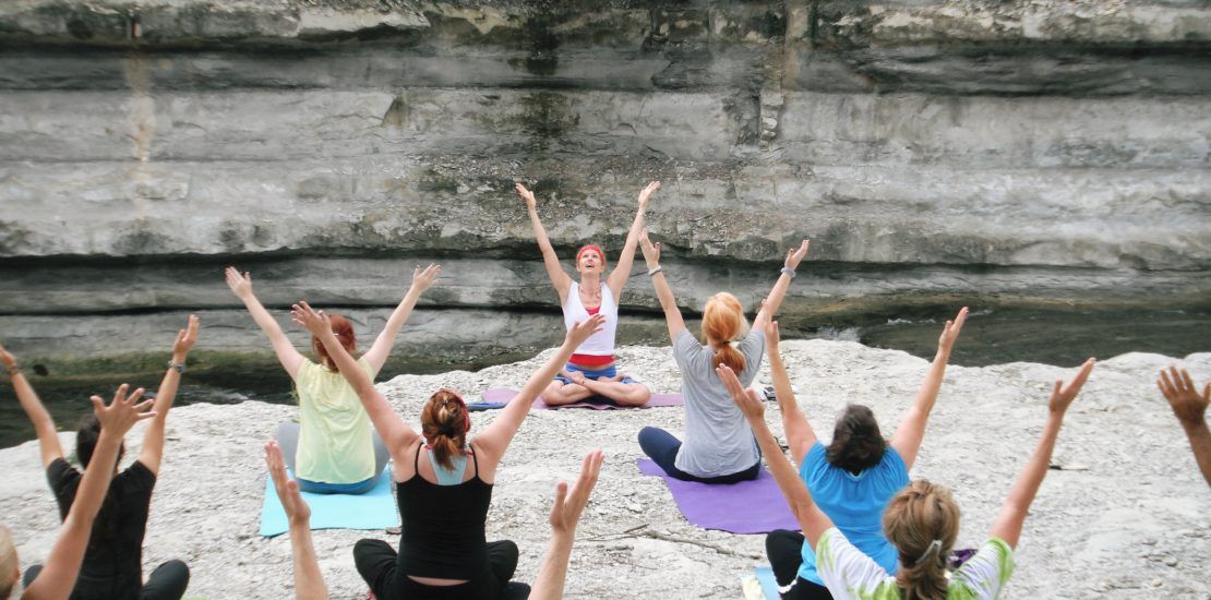 A group of people are doing yoga on the beach with their arms in the air.