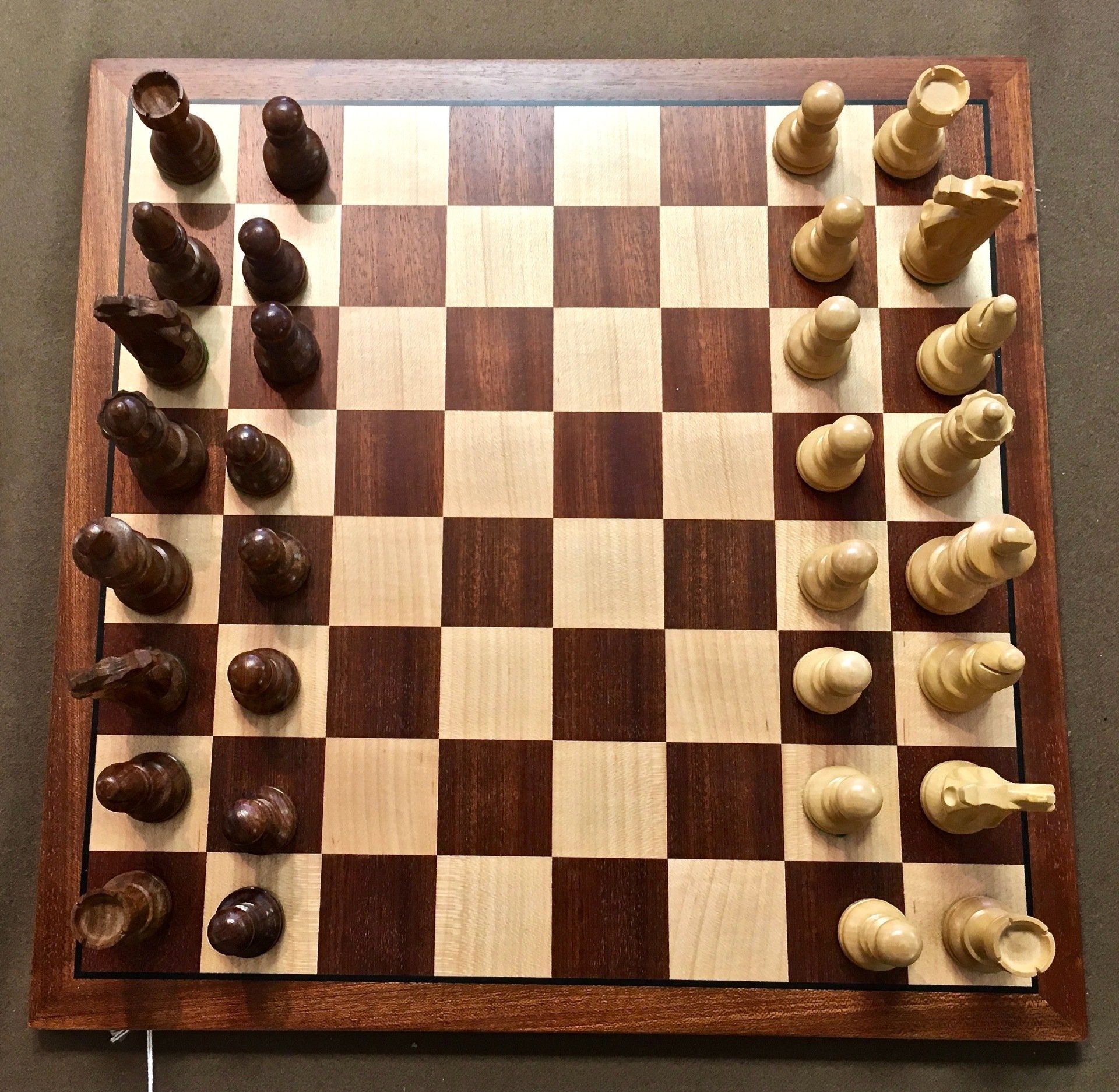 Wooden chessboard with black pieces on the left and white pieces on the right, game set up for play